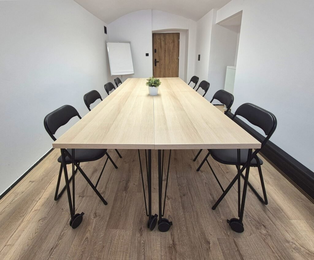 Sala lumen – rozmowy 1:1 Kameralna sala lumen o konstrukcji 12 m², stoły i krzesła w układzie do spotkań 1:1, regulowane oświetlenie, dźwiękoszczelne drzwi, klimat sprzyjający coachingowi w Krakowie